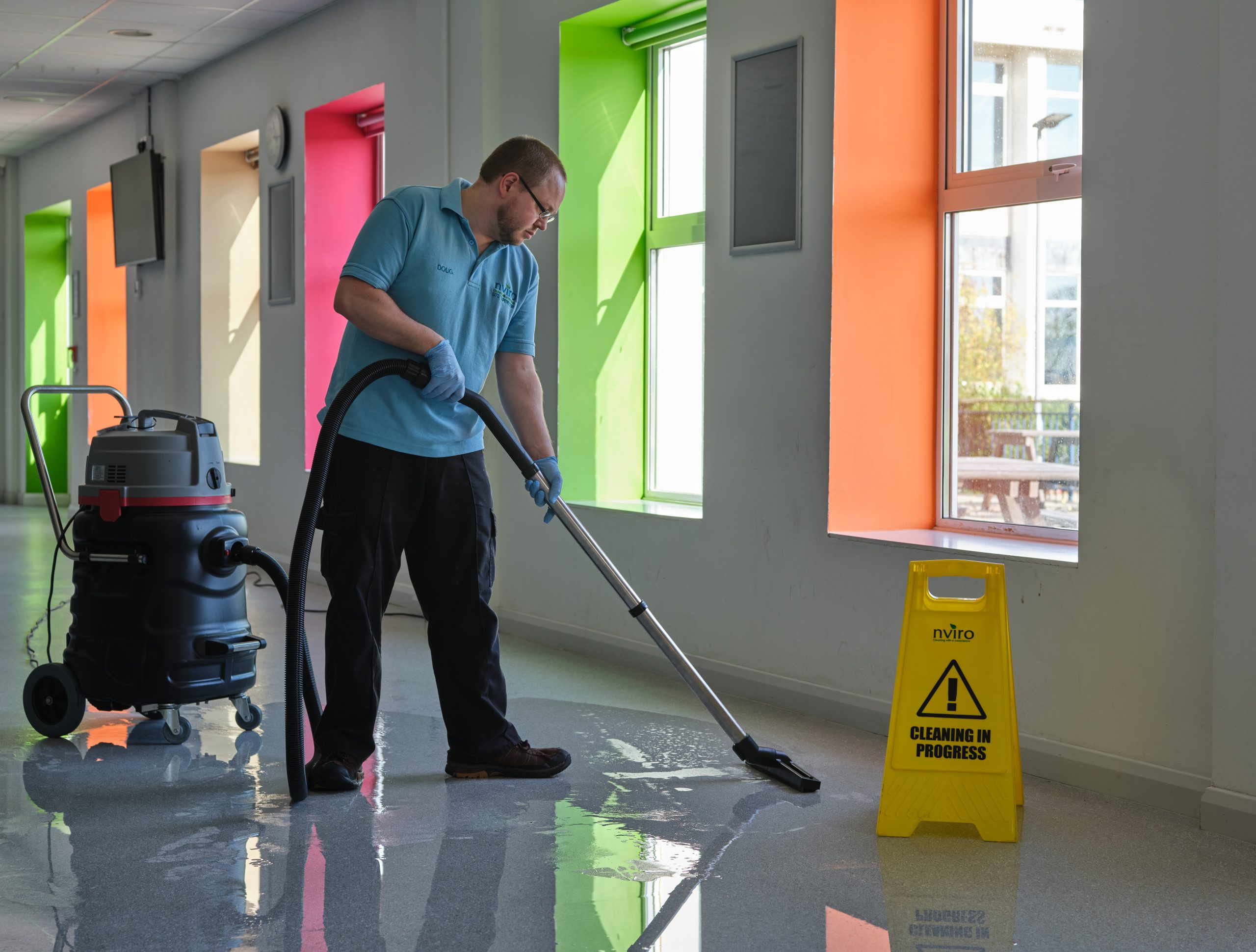 Cleaner using a wet pick up to remove water from room next to wet floor sign