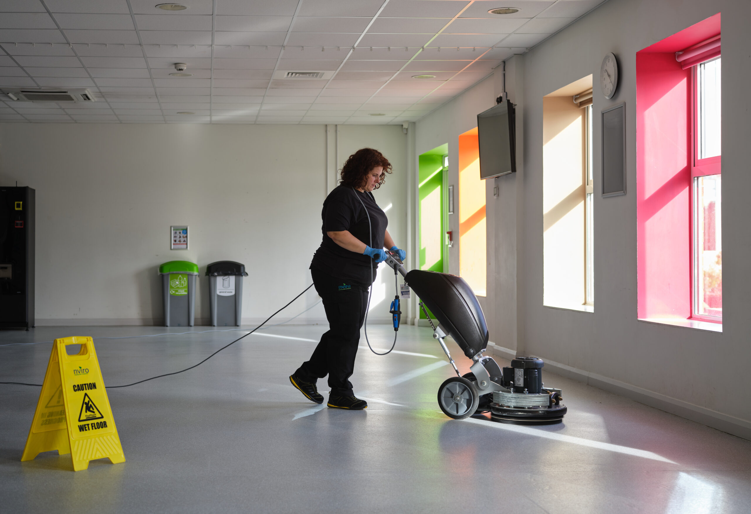 Cleaner pushing floor cleaning machine in open room near window